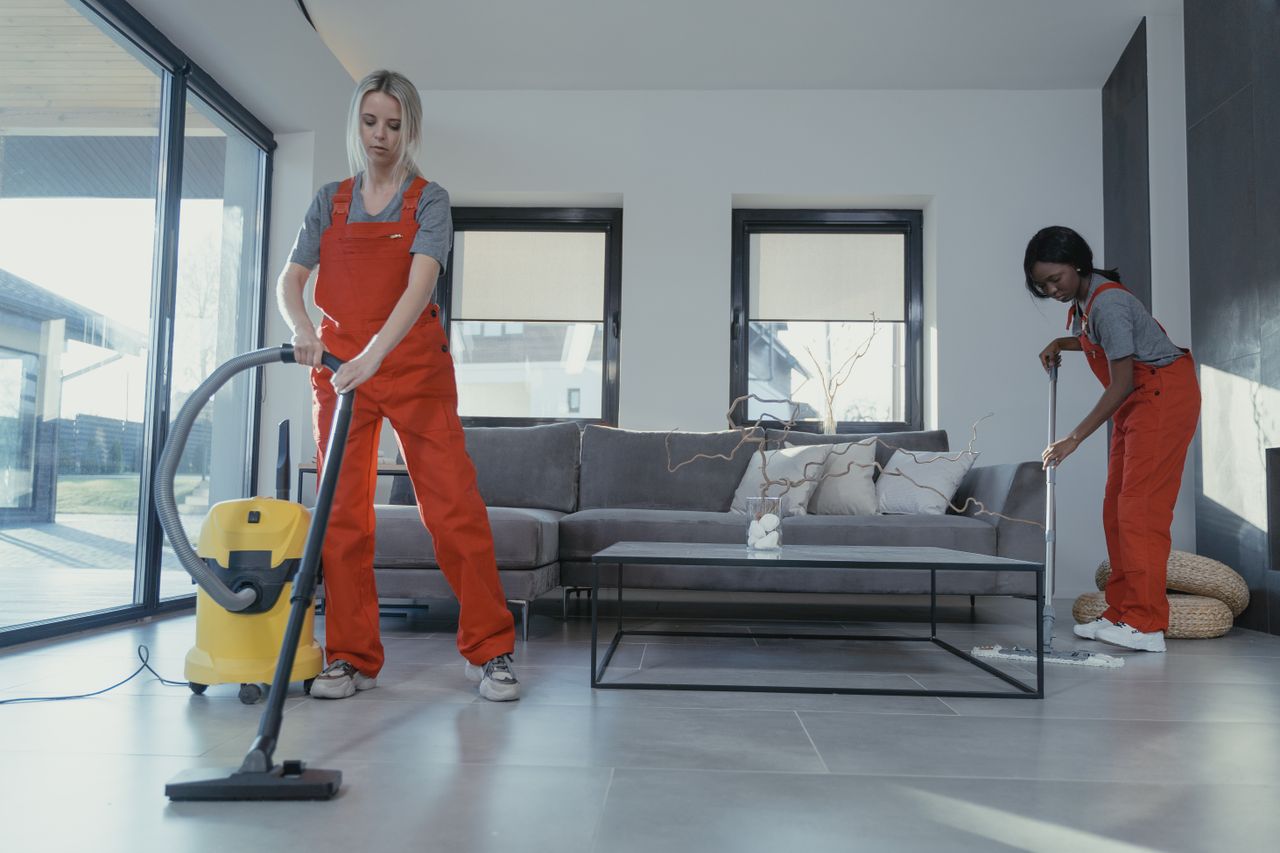 services-04 Two women wearing red overalls are vacuuming and sweeping a contemporary living room.